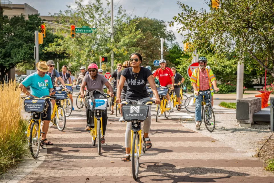 Group of people riding Pacers Bikeshare bikes on a tree-lined paved path.